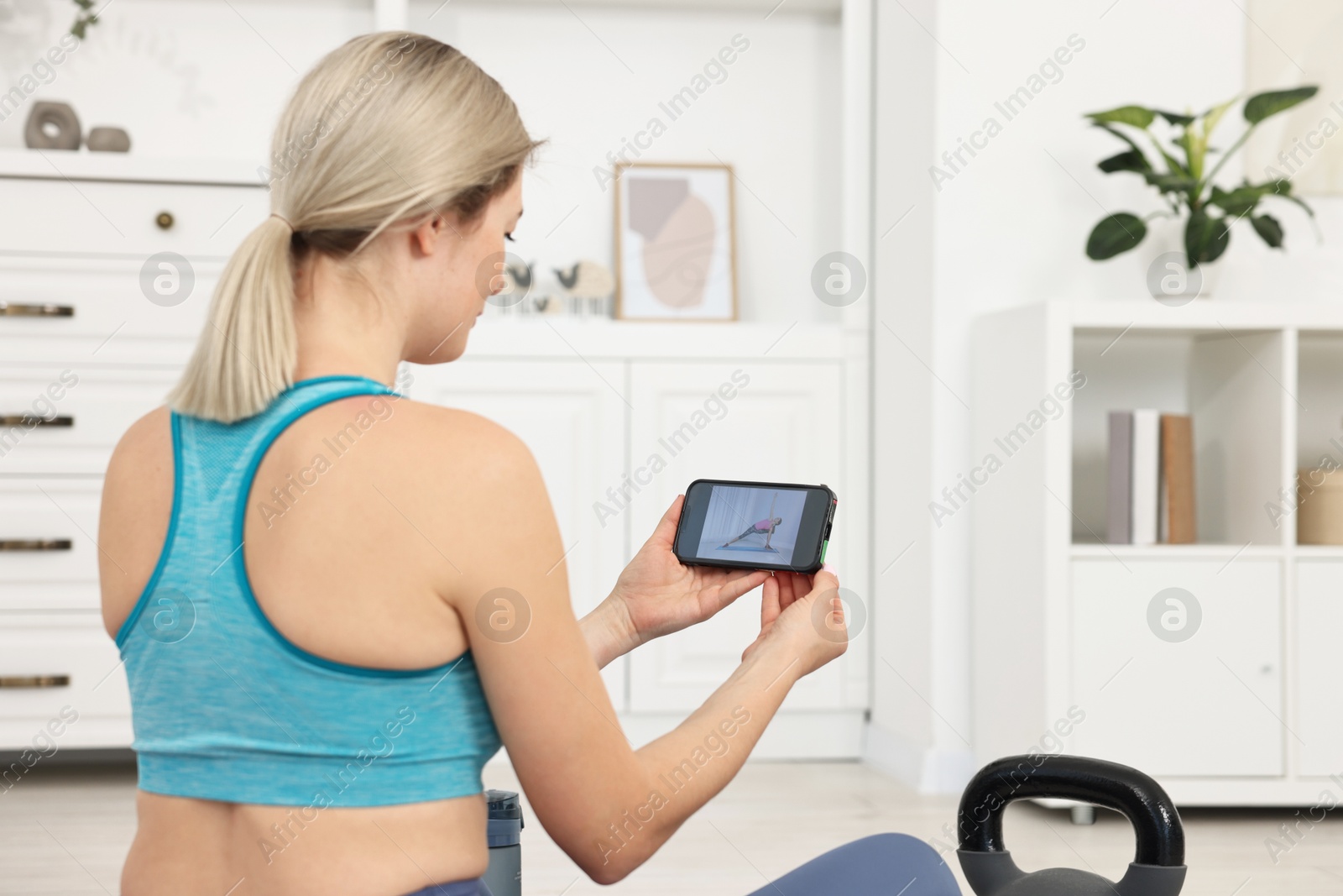 Photo of Online fitness trainer. Woman watching tutorial on smartphone at home