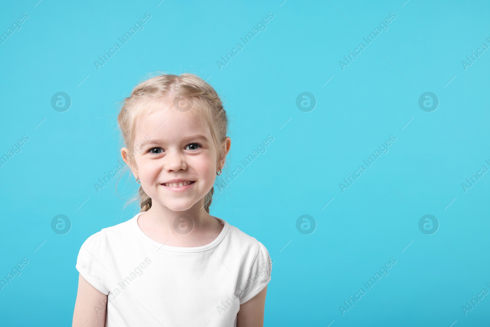 Photo of Portrait of cute little girl on light blue background, space for text