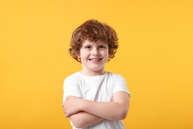 Portrait of cute little boy with crossed arms on orange background