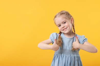 Photo of Cute little girl showing thumbs up on orange background, space for text