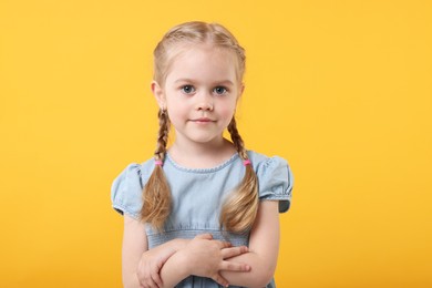 Portrait of cute little girl with crossed arms on orange background