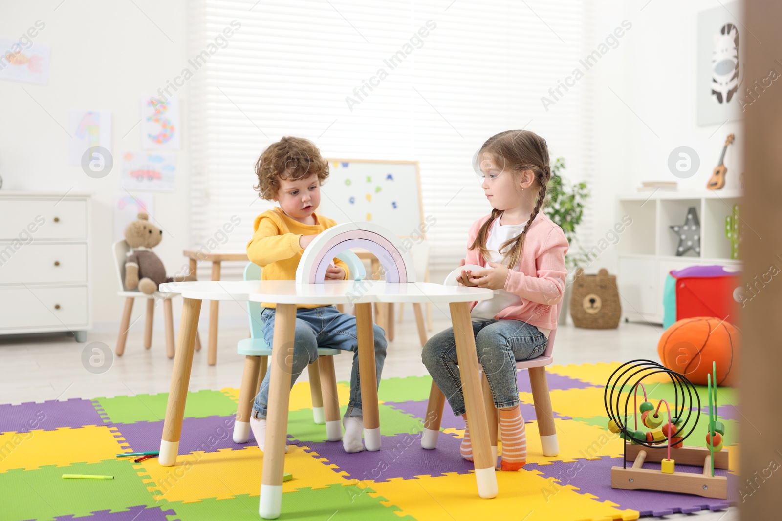 Photo of Cute little children playing with colorful toy rainbow at white table in kindergarten