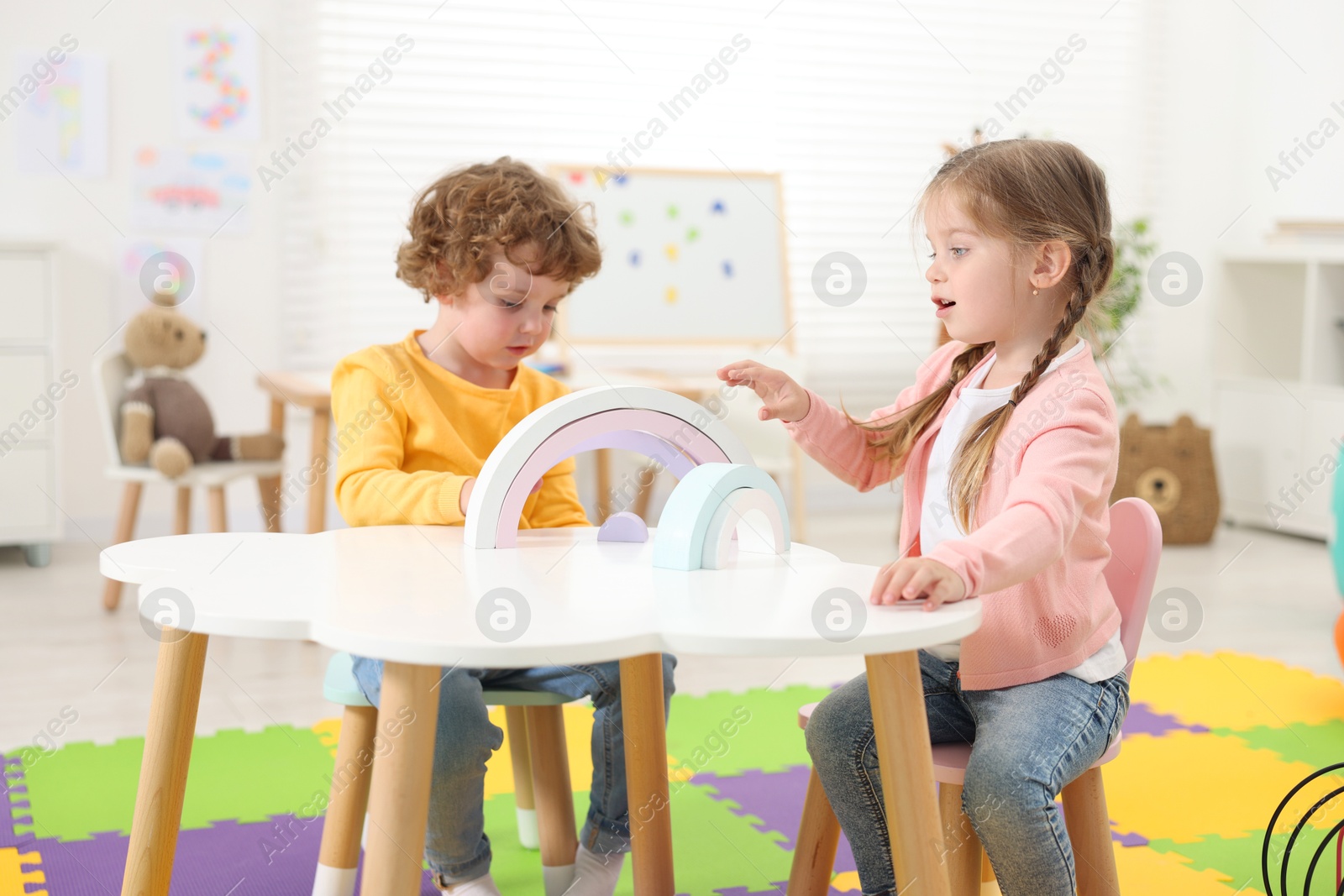 Photo of Cute little children playing with colorful toy rainbow at white table in kindergarten