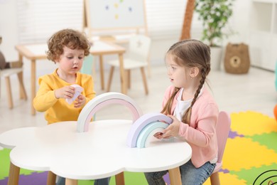 Cute little children playing with colorful toy rainbow at white table in kindergarten