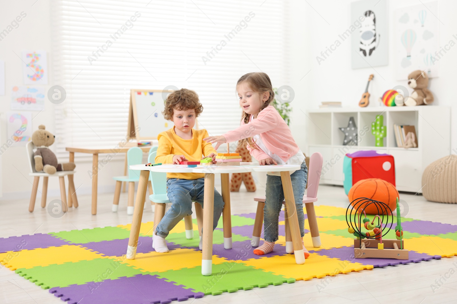 Photo of Cute little children playing with colorful toy pyramid at white table in kindergarten