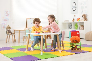 Photo of Cute little children playing with colorful toy pyramid at white table in kindergarten