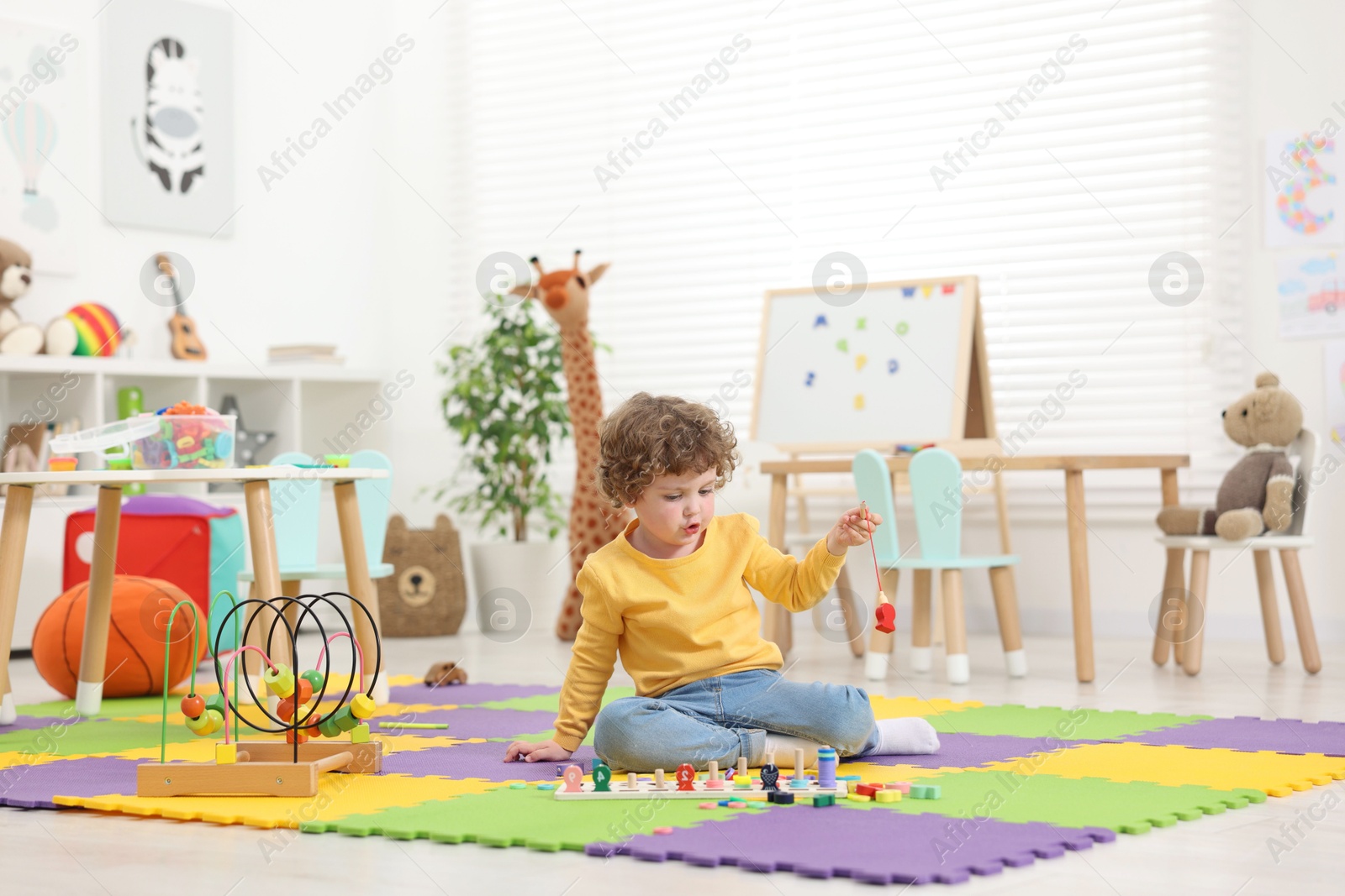 Photo of Cute little boy playing with math game Fishing for Numbers on puzzle mat in kindergarten