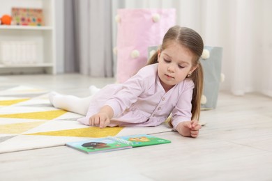 Cute little girl reading book on floor in kindergarten