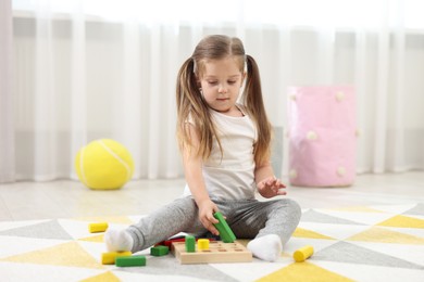 Photo of Cute little girl playing with set of wooden geometric figures on floor in kindergarten