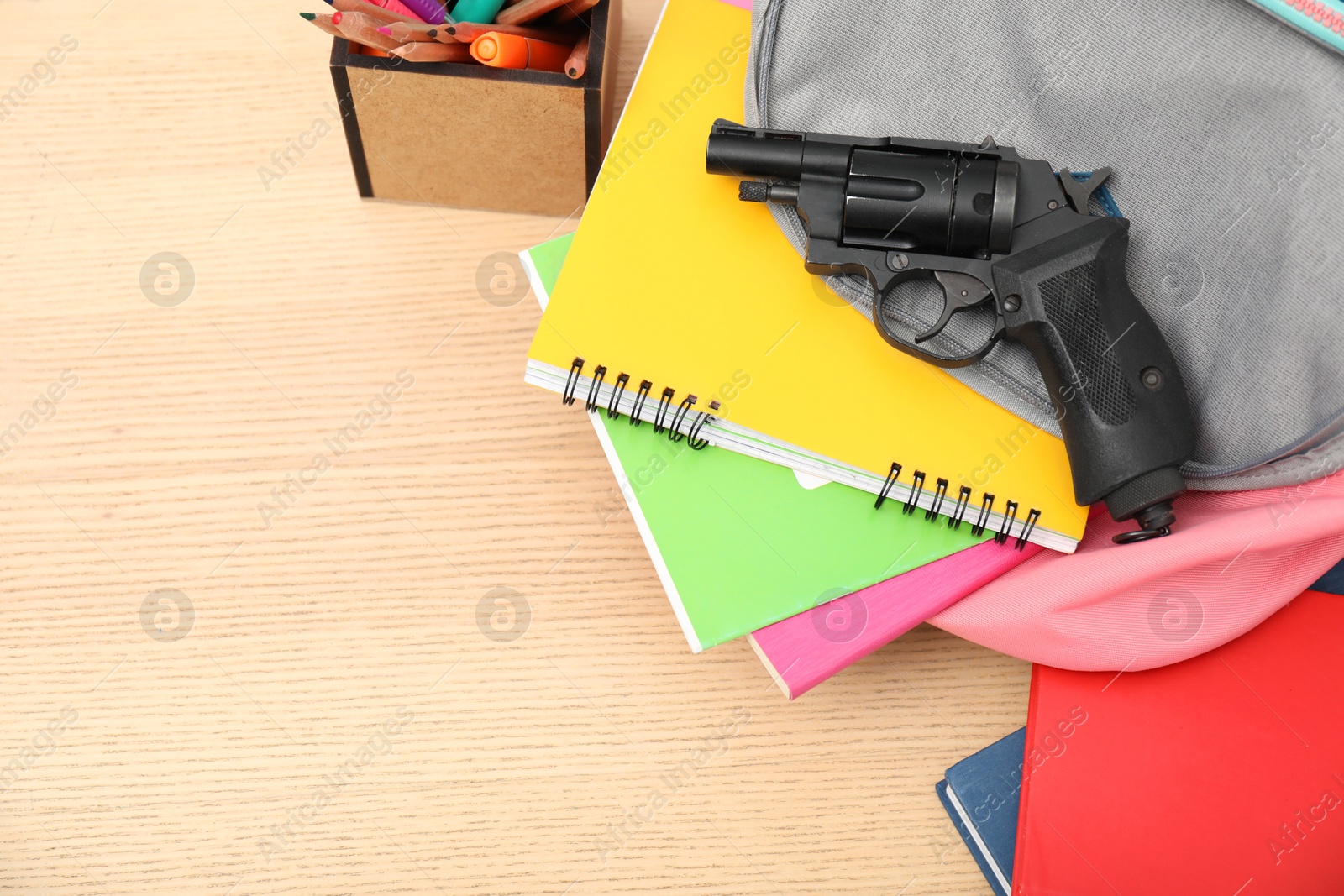 Photo of School stationery, gun and backpack on wooden desk, above view. Space for text