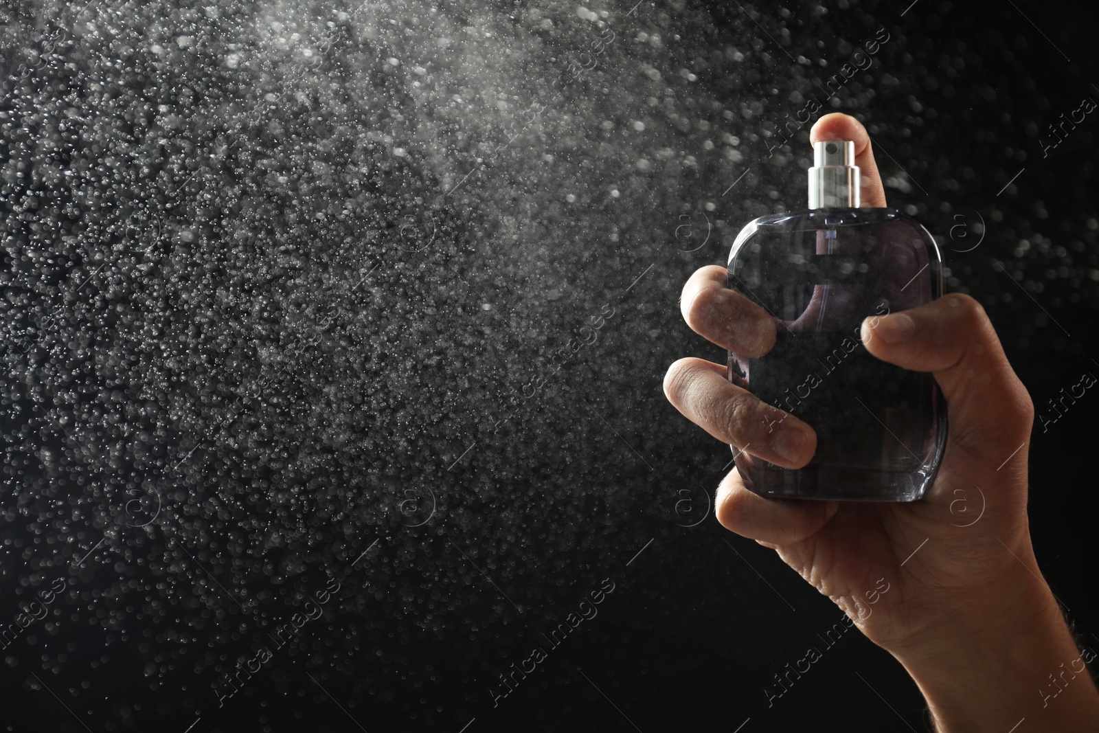 Photo of Man spraying luxury perfume on dark background, closeup. Space for text