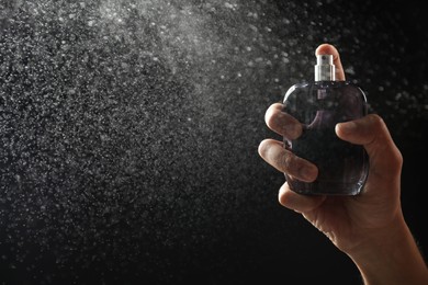 Man spraying luxury perfume on dark background, closeup. Space for text