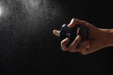 Man spraying luxury perfume on dark background, closeup. Space for text