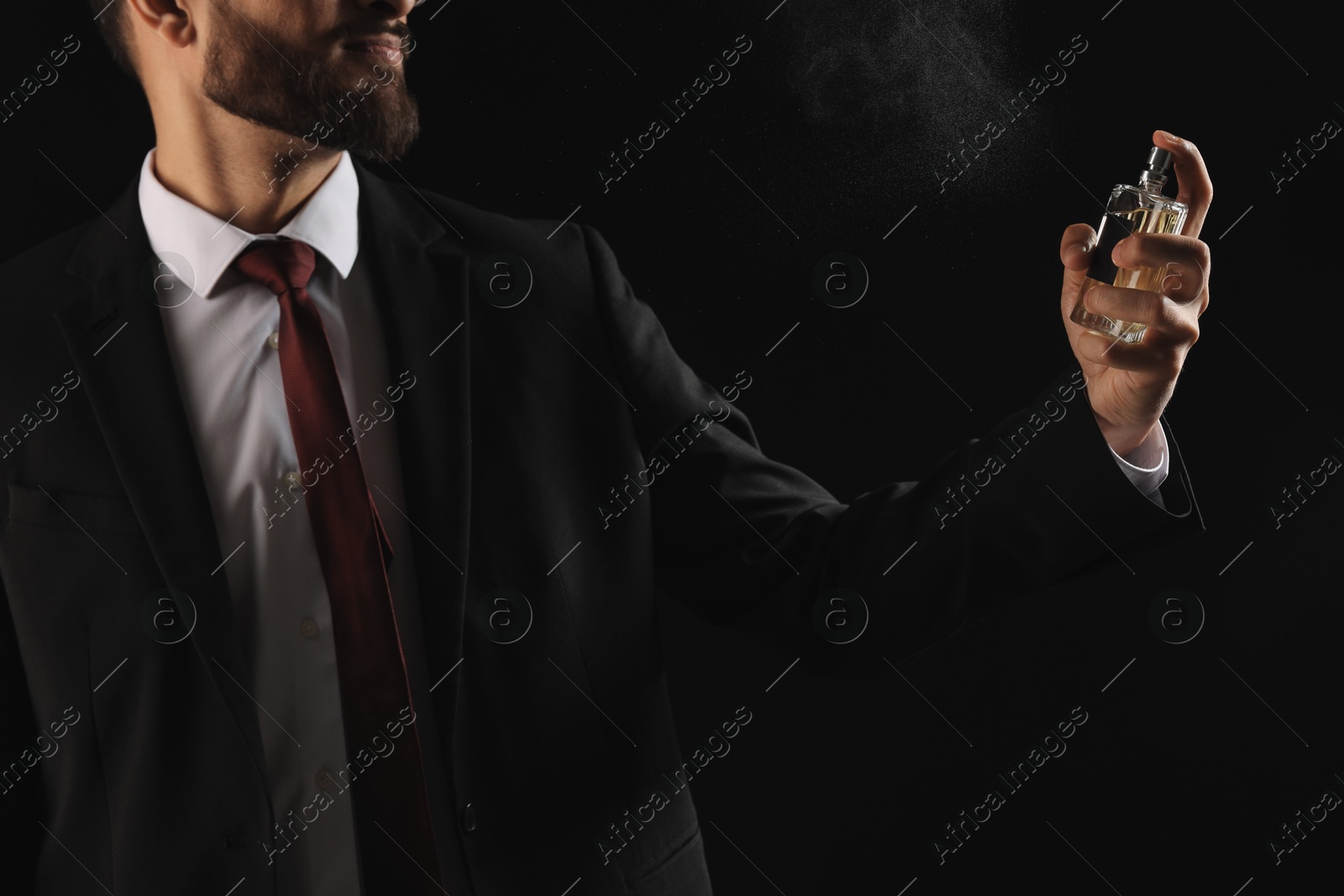 Photo of Man spraying luxury perfume on dark background, closeup