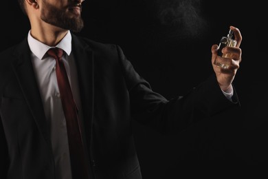 Photo of Man spraying luxury perfume on dark background, closeup