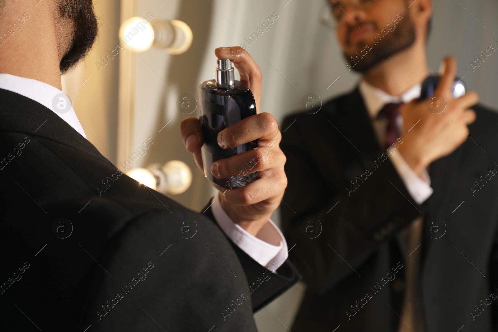 Photo of Man spraying luxury perfume near mirror indoors, closeup