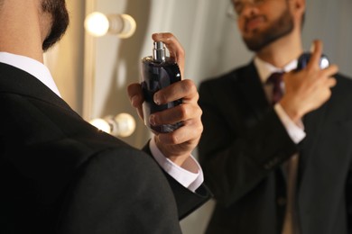 Man spraying luxury perfume near mirror indoors, closeup