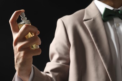 Photo of Man spraying luxury perfume on dark background, closeup