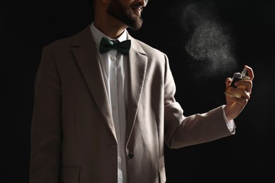 Man spraying luxury perfume on dark background, closeup