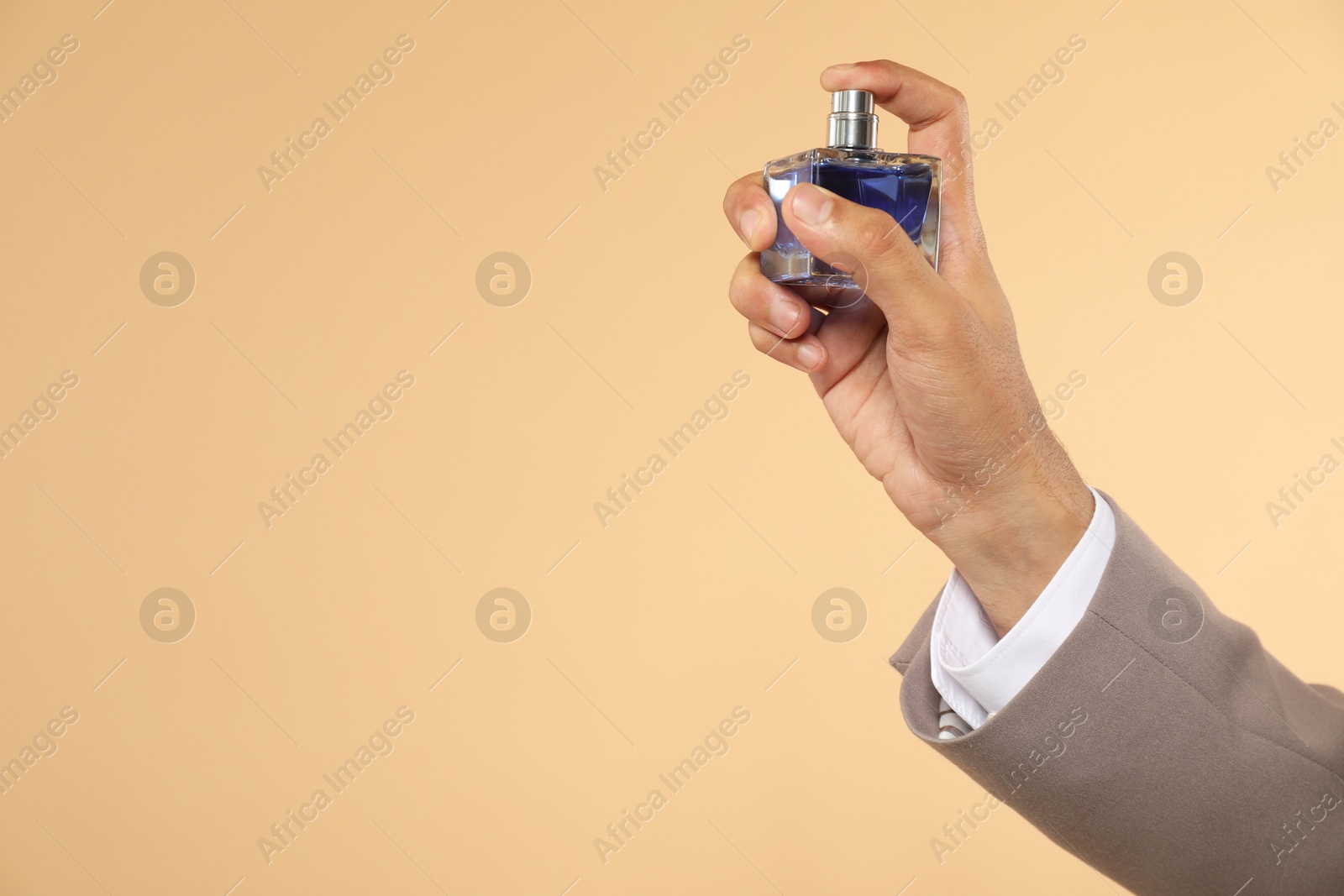 Photo of Man spraying luxury perfume on beige background, closeup. Space for text