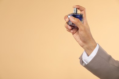 Man spraying luxury perfume on beige background, closeup. Space for text