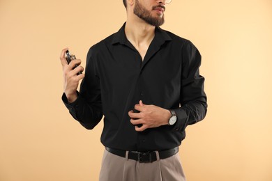 Photo of Man spraying luxury perfume on beige background, closeup