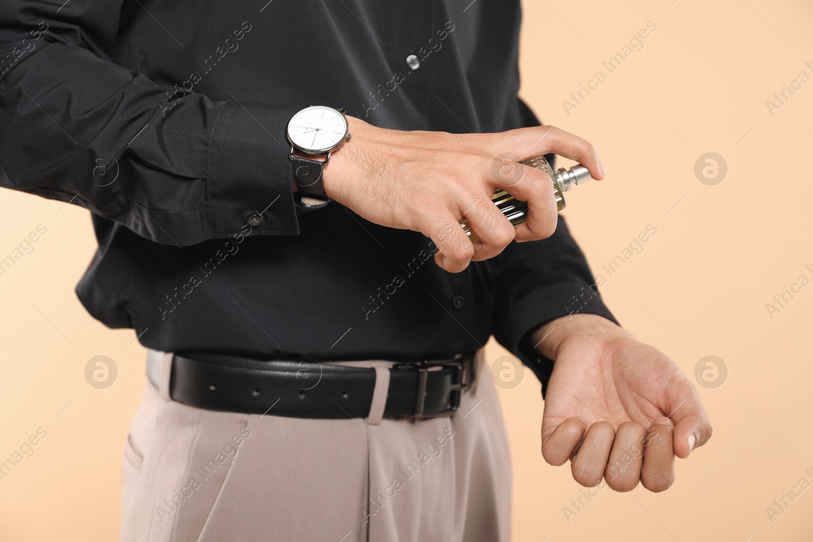 Photo of Man spraying luxury perfume on beige background, closeup