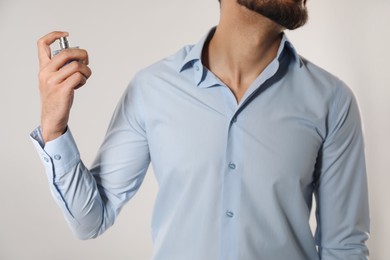 Man spraying luxury perfume on light background, closeup