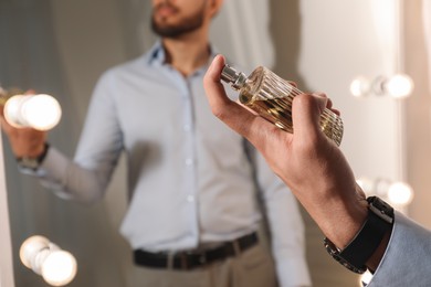 Man spraying luxury perfume near mirror indoors, closeup