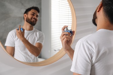 Photo of Man spraying luxury perfume near mirror indoors