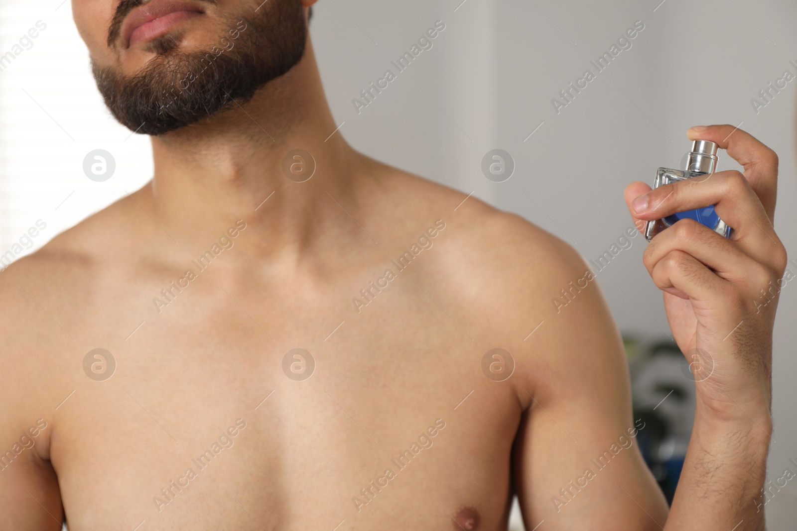 Photo of Young man spraying luxury perfume indoors, closeup