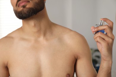 Photo of Young man spraying luxury perfume indoors, closeup