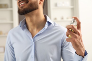 Young man spraying luxury perfume indoors, closeup