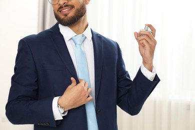 Photo of Young man spraying luxury perfume indoors, closeup