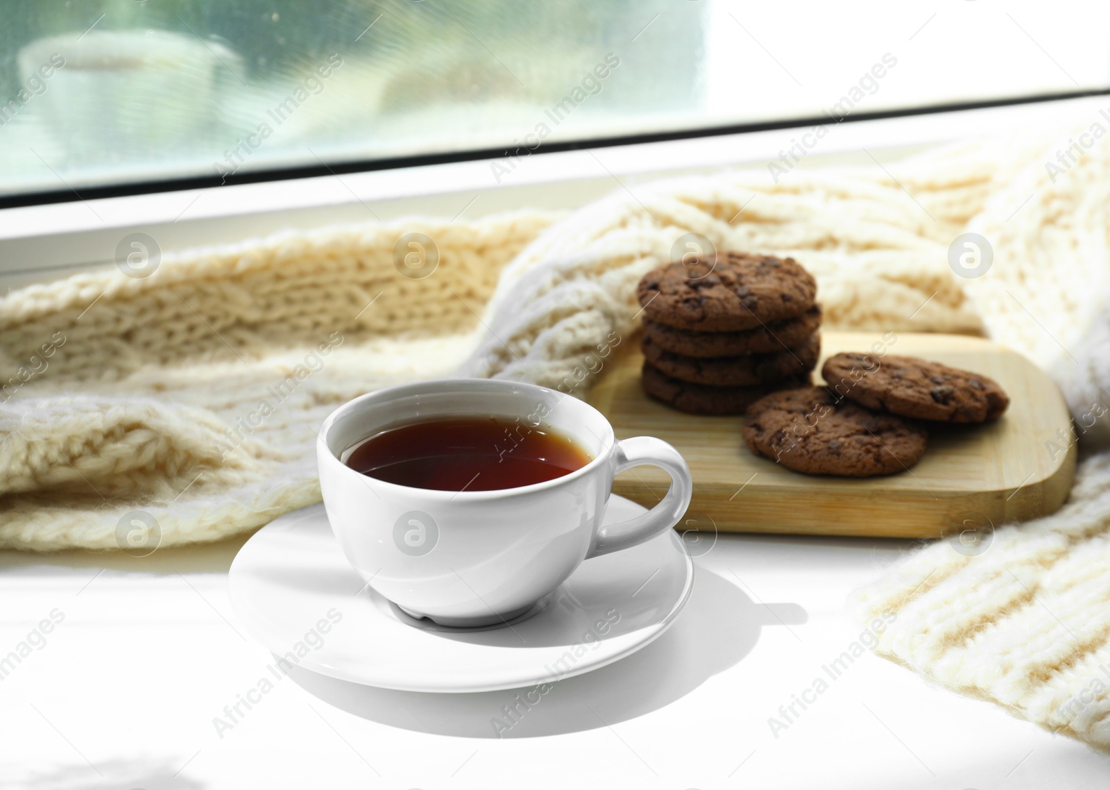Photo of Beige knitted scarf, tea and cookies on windowsill