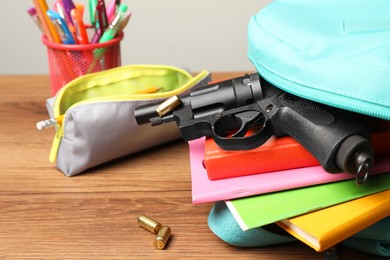 Photo of Gun, bullets and school stationery on wooden table , closeup
