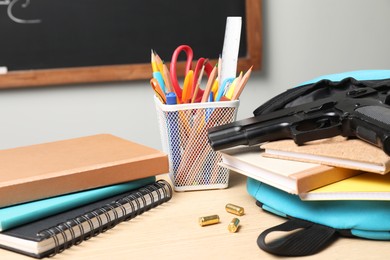 Photo of Gun, bullets and school stationery on wooden table near blackboard indoors, closeup