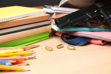 Photo of Gun, bullets and school stationery on wooden table, closeup