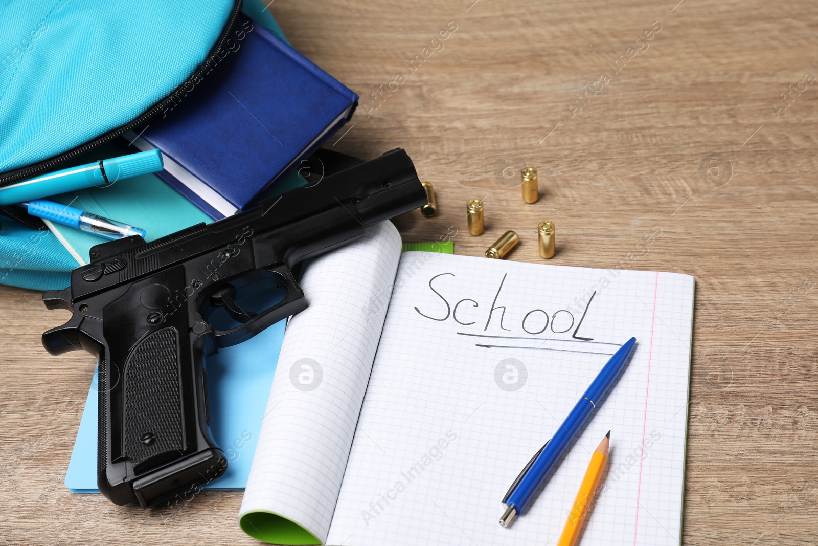 Photo of Gun, bullets and school stationery on wooden table, above view