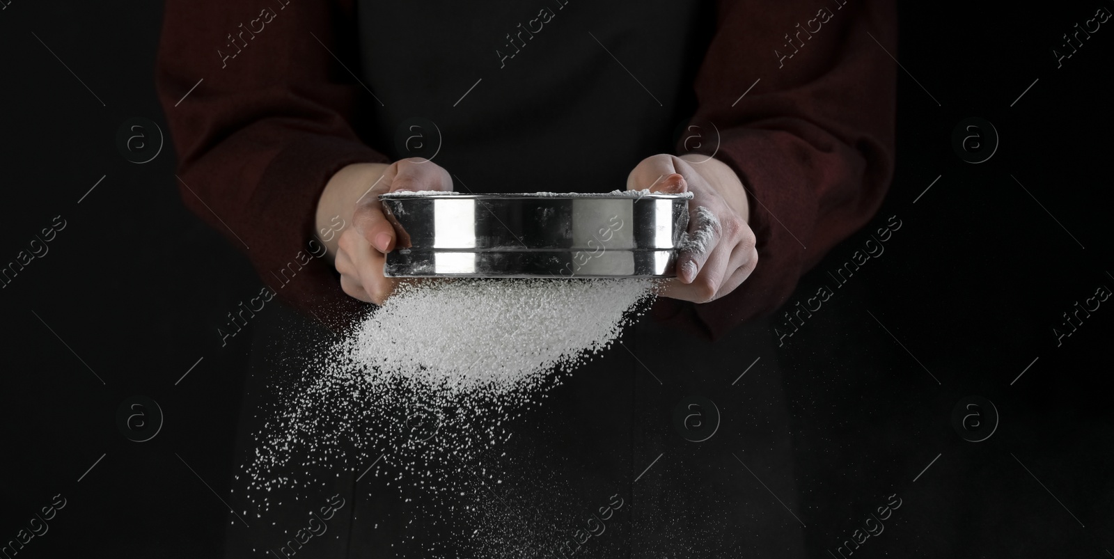 Photo of Woman sieving flour at table against black background, closeup