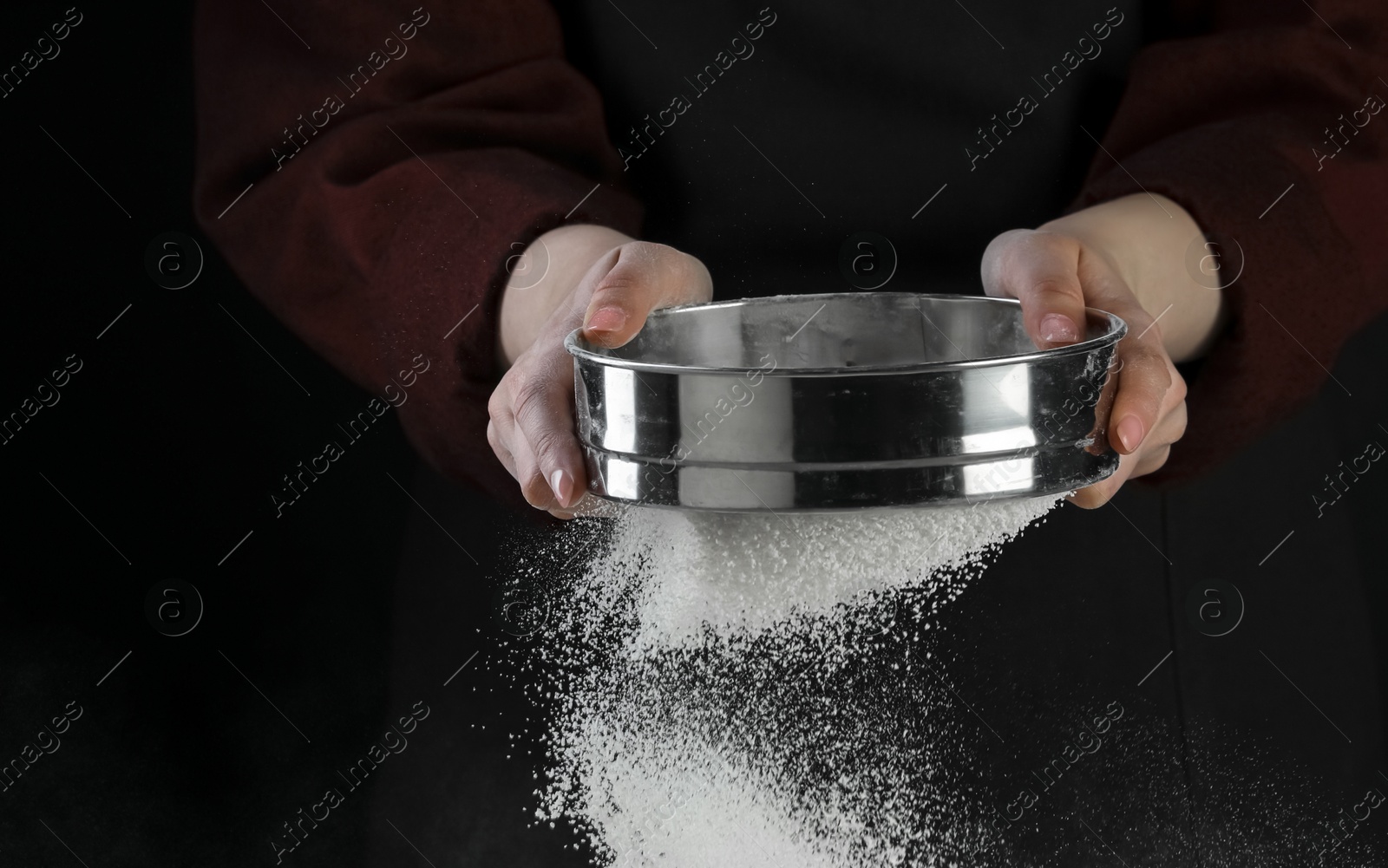 Photo of Woman sieving flour against black background, closeup