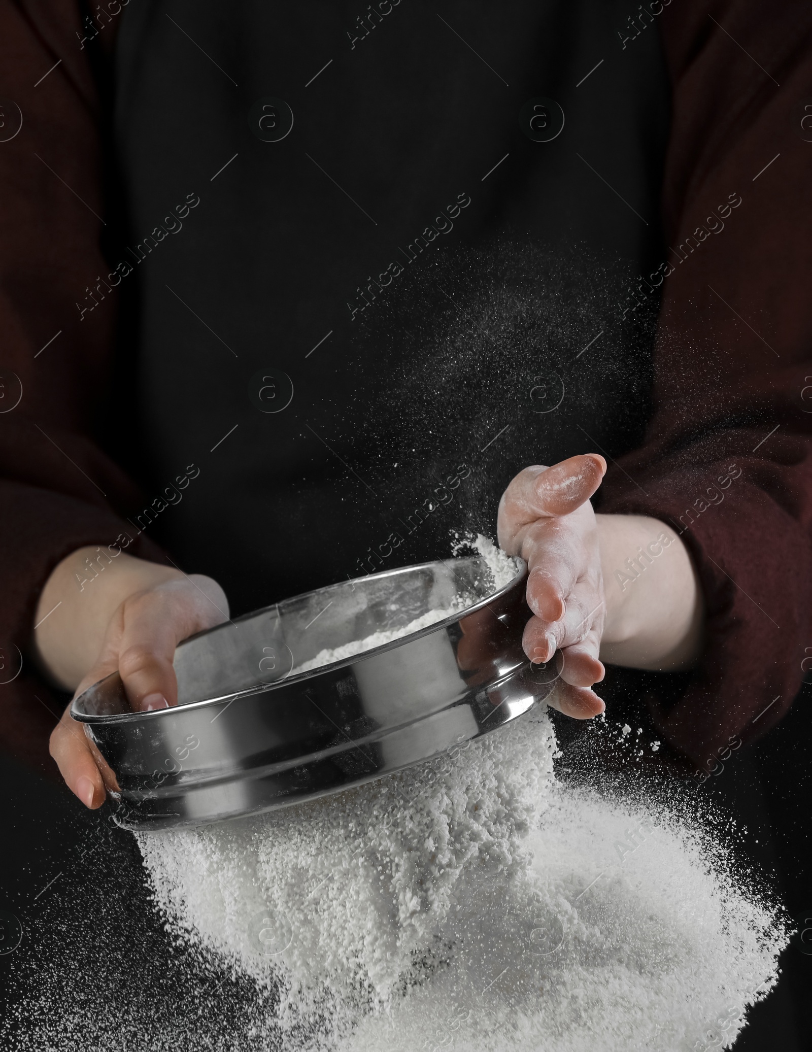 Photo of Woman sieving flour against black background, closeup