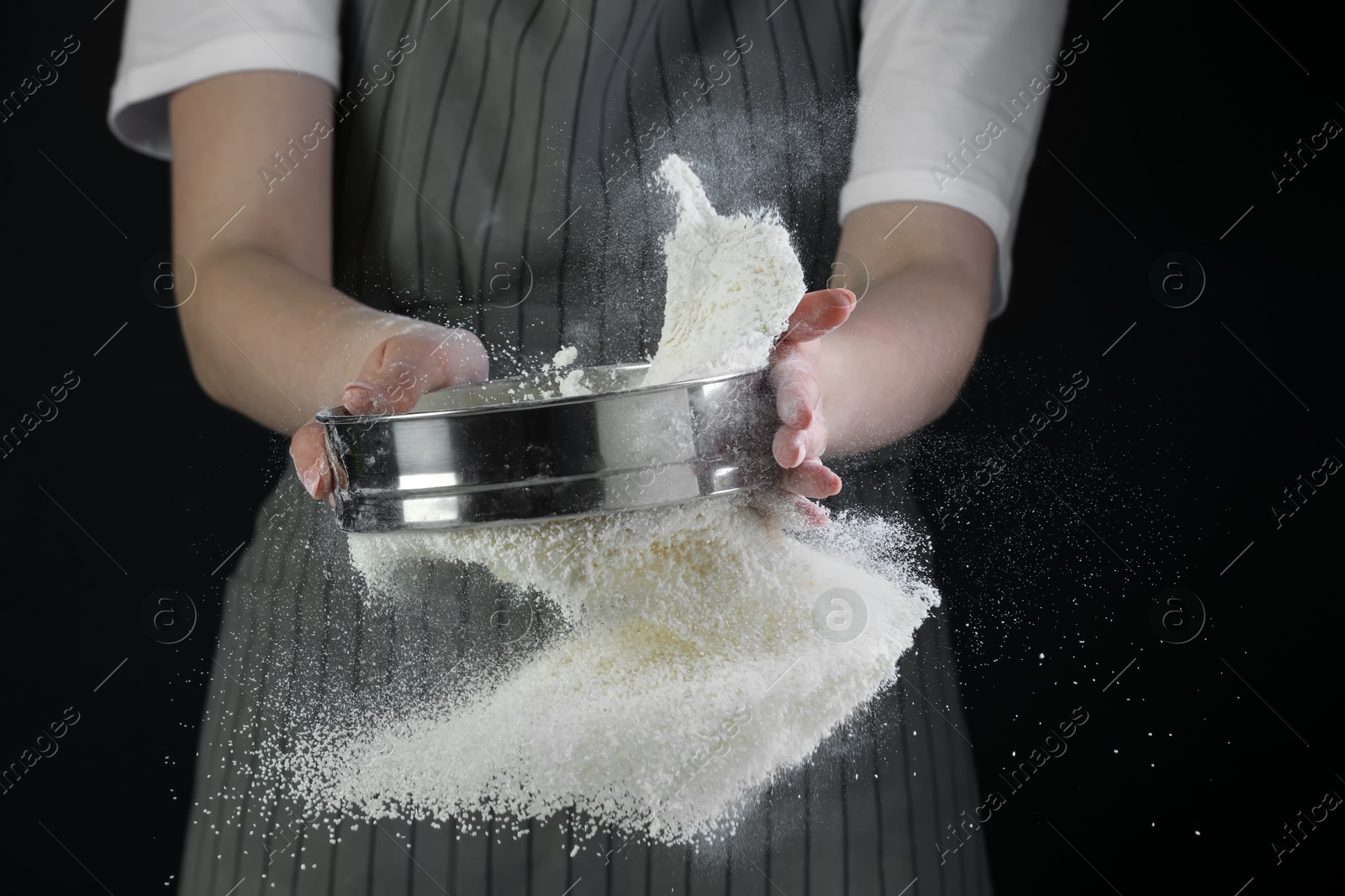 Photo of Woman sieving flour against black background, closeup