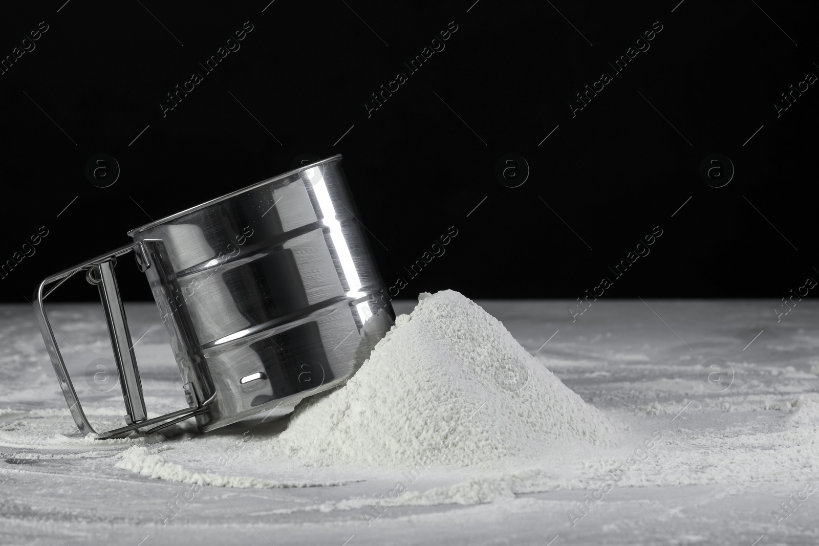 Photo of Sifter and pile of flour on grey table against black background