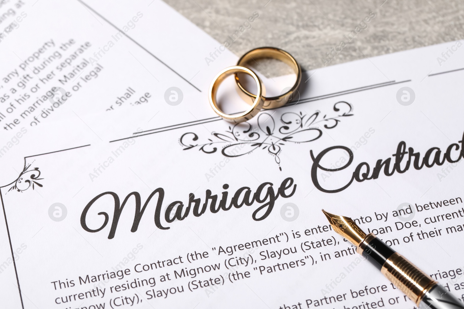 Photo of Marriage contract, fountain pen and golden wedding rings on grey table