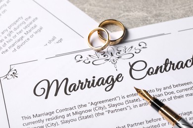 Marriage contract, fountain pen and golden wedding rings on grey table