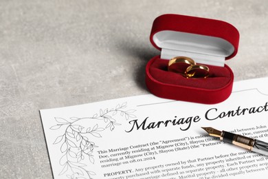 Photo of Marriage contract, fountain pen and golden wedding rings on grey table