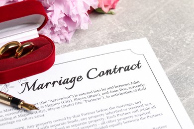 Marriage contract, fountain pen, golden wedding rings and flowers on grey table, closeup