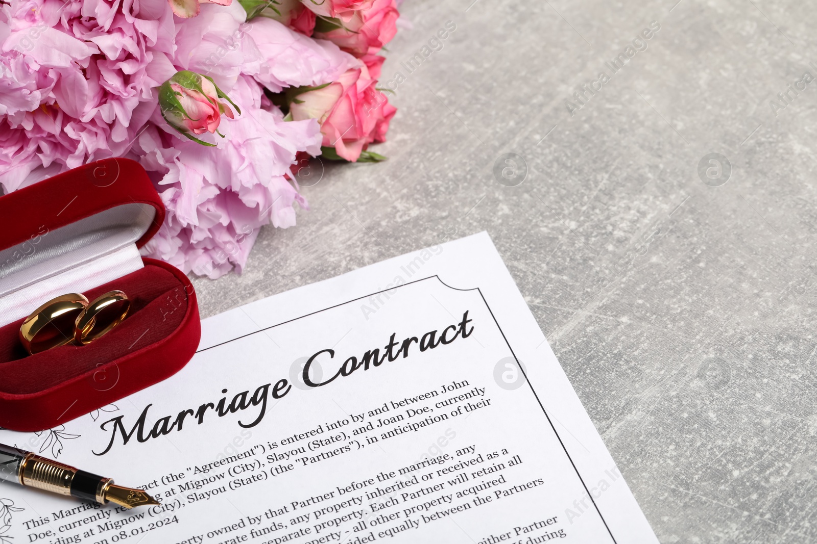 Photo of Marriage contract, fountain pen, golden wedding rings and flowers on grey table