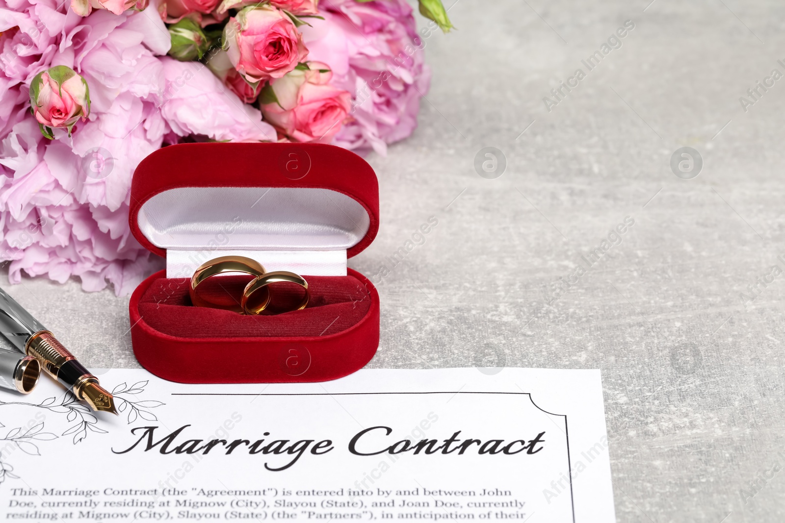 Photo of Marriage contract, fountain pen, golden wedding rings and flowers on grey table